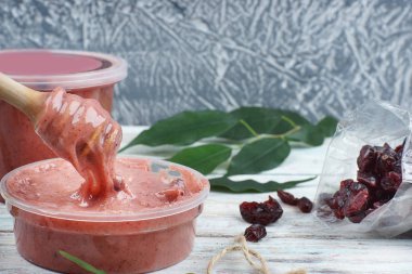 Masanın üzerinde pembe renkli çırpılmış bal, bal için kaşık değirmeni, kese içinden dökülen kurumuş böğürtlen.