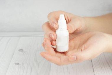Hands of a young girl with beautiful skin hold in their palms a small white bottle with cosmetic or perfumery