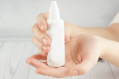 The hands of a young girl hold in their palms a large white bottle with cosmetic or perfumery, copy space for your text on the left