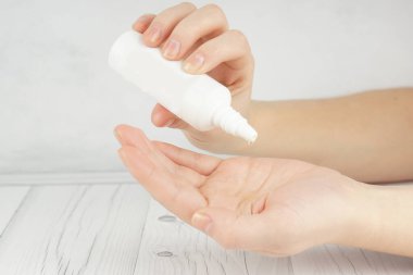 A young girl holds in her palms a large white bottle with cosmetic or perfume, drips into her palm, copy space for your text on the left