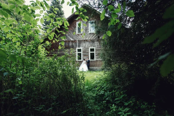 Bride and groom by old wooden house — Stock Photo, Image