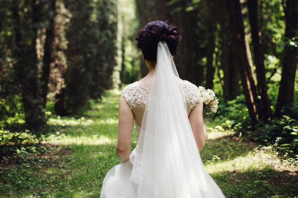 Veil hangs from bride's head while she walks through the wood