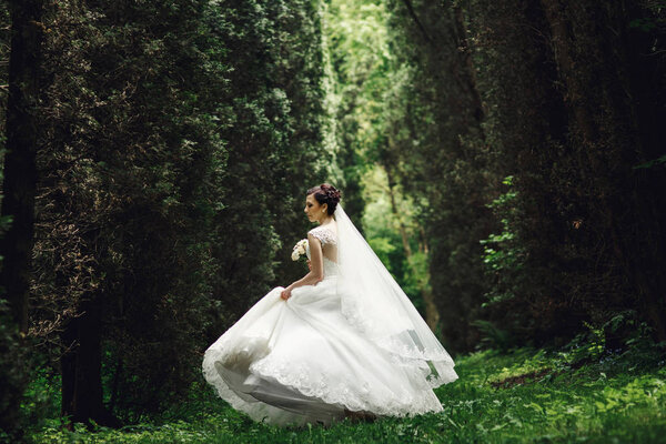 Delicious bride holds her dress while she whirls in the forest