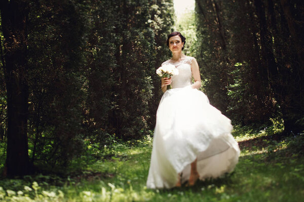 Magnificent bride holds her dress while she walks cross the dense forest
