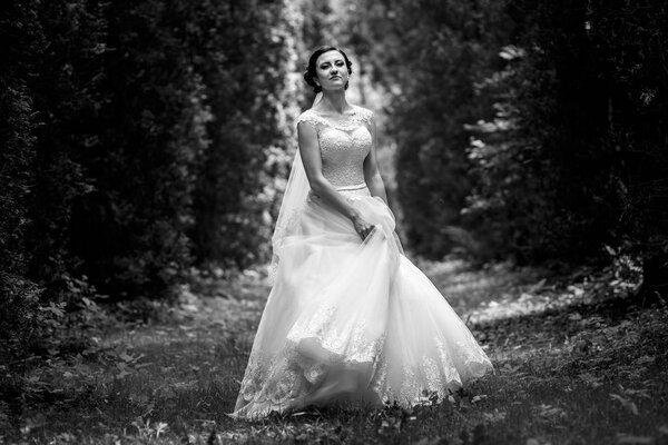 Thick forest surrounding gorgeous bride whirling on the path, black and white photo