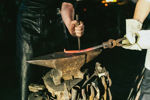Groom holds hot steel for blacksmith — Stock Photo, Image