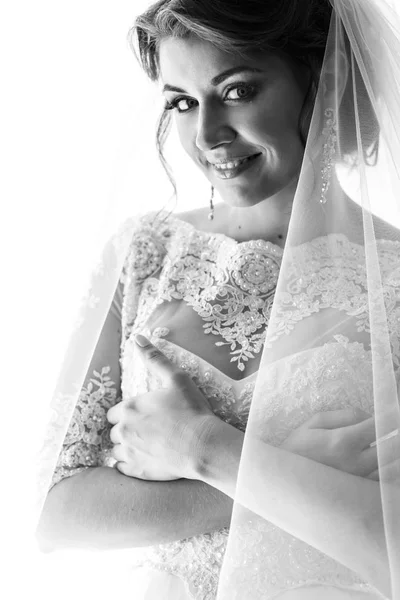 Elegante bruid in lace gown door raam — Stockfoto