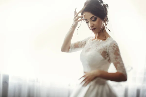 Elegante bruid in lace gown door raam — Stockfoto