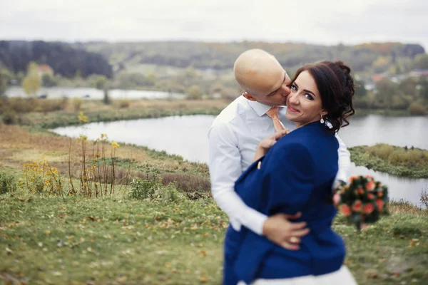 Recém-casados abraçando por lago de outono — Fotografia de Stock