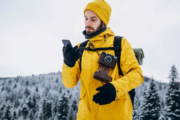 Man in yellow suit talks on the phone walking around the mountains covered with snow