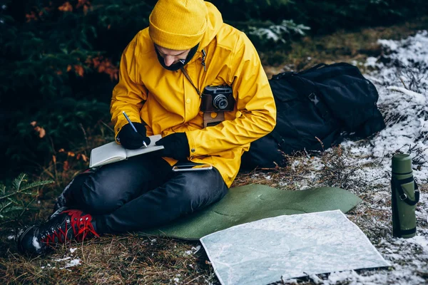 Man takes notes sitting with map on the ground somewhere in the winter forest