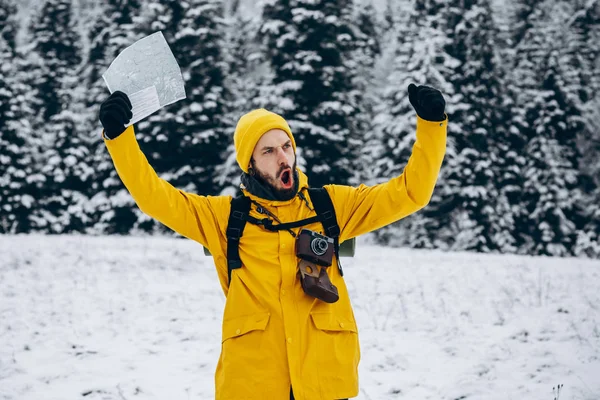 Happy man in yellow jacket jumps on the snow with a map in his arms somwhere in the mountains