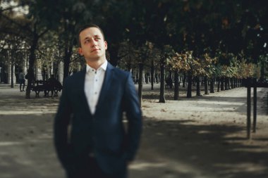 Yakışıklı adam koyu takım elbiseli bir parkta güneşli bir yerde Paris standları