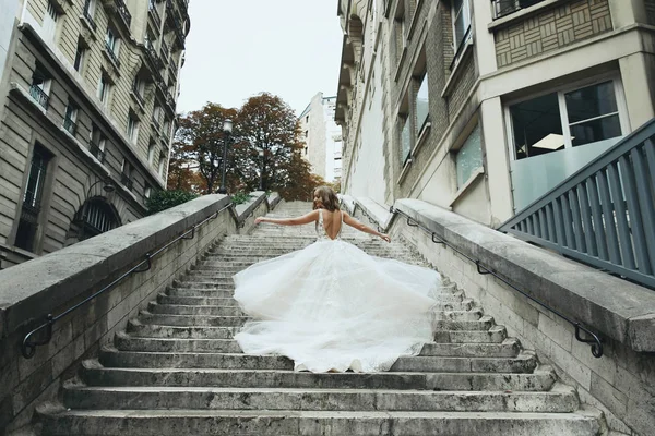 Blonde bride in luxury wedding dress whirls on footsteps somewhere in Paris