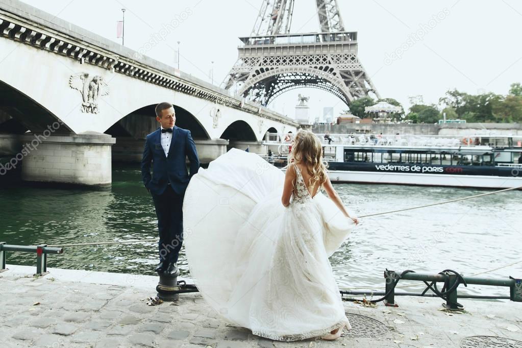 Luxury wedding couple poses before river Seine and the Eiffel Tower somewhere in Paris