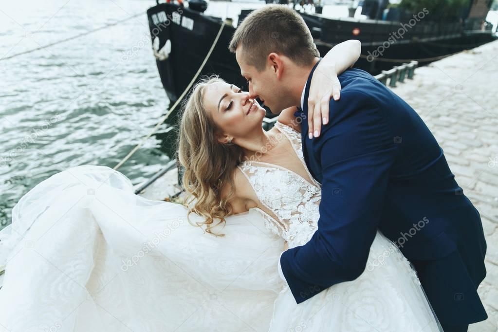 Classy groom and bride in luxurious dress pose before the river Seine somewhere in Paris