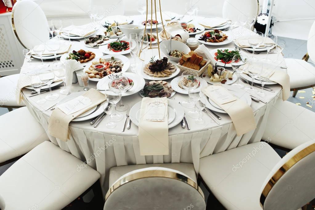 White soft chairs with golden design stand at the dinner table served for wedding party