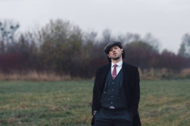 Eski moda siyah takım elbiseli ve göz kamaştırıcı bir şey söyleyen ellerini ceplerine sokup kameraya bakan sevimli bir adam. Moda ve bağbozumu kavramı.