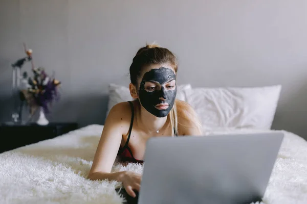 Woman with mud mask using laptop in bedroom — Stock Photo, Image