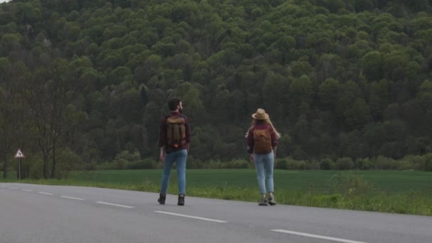 Pareja camina a lo largo de la carretera y mira el coche — Vídeos de Stock