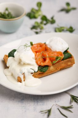 Haşlanmış yumurtalı waffle ve beyaz tabakta somon.