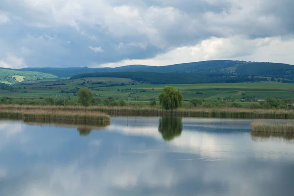 Vista panorâmica para o lago Rotbav, resort turístico com colinas no fundo em um dia ensolarado de primavera com céu azul nublado Rotbav, Romênia, Europa — Fotografia de Stock