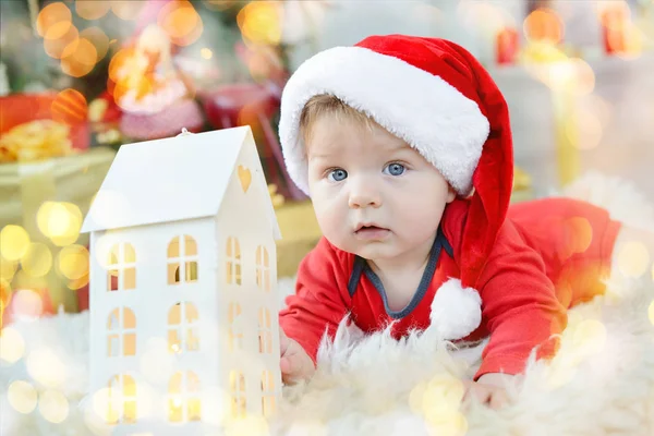 肖像的漂亮小宝贝庆祝圣诞节。新的一年的假期。圣诞老人服装与玩具房子在树下的男孩 — 图库照片