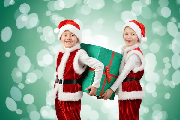 Entzückende glückliche Jungen in Weihnachtsmannkleidung, die eine Weihnachtsgeschenkbox in der Hand halten. isoliert auf grünem Hintergrund mit Lichtern. — Stockfoto