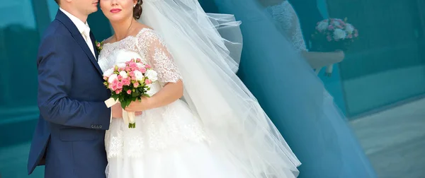 Pasangan pengantin memegang karangan bunga merah muda dan mawar putih di latar belakang biru — Stok Foto