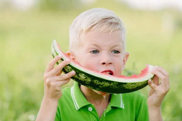Engraçado menino com cabelos loiros comendo melancia ao ar livre . — Fotografia de Stock