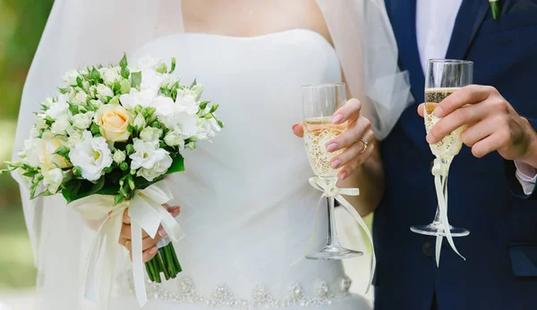 Pengantin pria dan wanita memegang gelas sampanye dan buket pernikahan dengan mawar putih — Stok Foto
