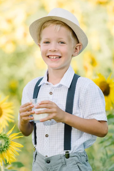 Adorable niño rubio divertido comer bagel y beber leche en el campo de girasol de verano al aire libre — Foto de Stock