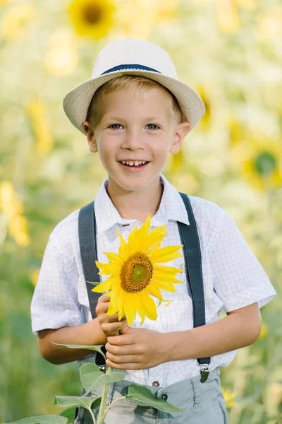 Chłopiec blond roześmiany w kapelusz ze słonecznikiem na zewnątrz pola — Zdjęcie stockowe