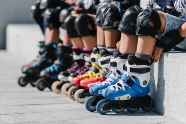 Feet of rollerbladers wearing inline roller skates sitting in outdoor skate park, Close up view of wheels befor skating clipart