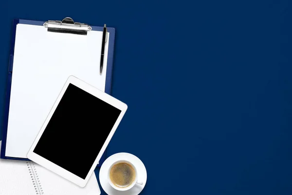 Bureau table de bureau avec ordinateur portable, tablette, tasse de café et carnet de notes vierge sur fond bleu . — Photo