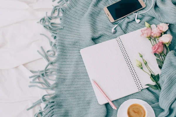 Toned Flat lay tablet, phone, cup of coffee and flowers on white blanket with turquoise plaid