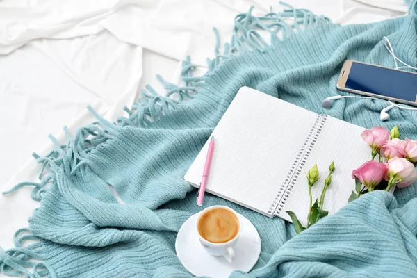 Flat lay tablet, phone, cup of coffee and flowers on white blanket with turquoise plaid