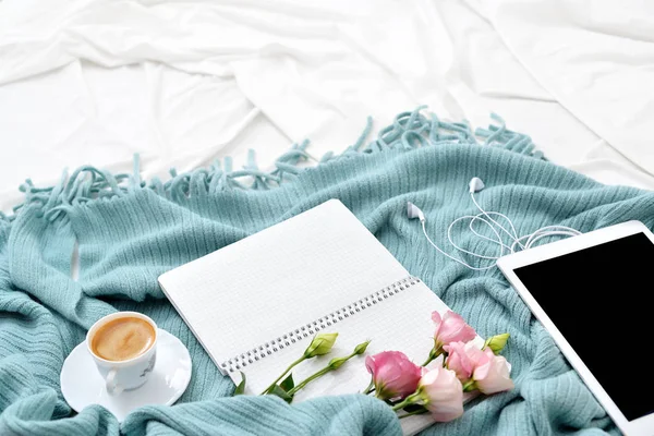 Плаский планшет, телефон, чашка кави та квіти на білій ковдрі з бірюзовою плед — стокове фото