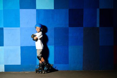 Sevimli küçük çocuğa tekerlekli paten ayakta mavi grafiti duvara karşı