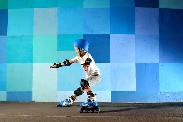 Jovem em patins fazendo slide contra a parede azul do graffiti — Fotografia de Stock