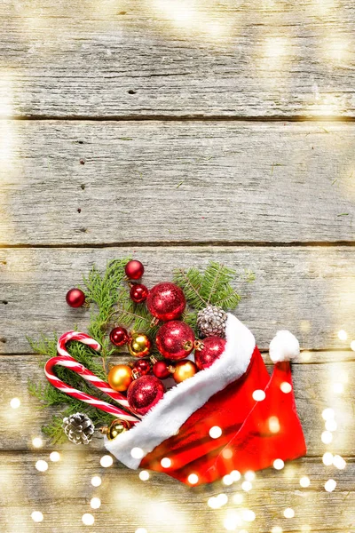 Červený klobouk santa claus s vánoční složení míče, hračky, sladkosti, jedlové větve na vinobraní dřevěné pozadí — Stock fotografie