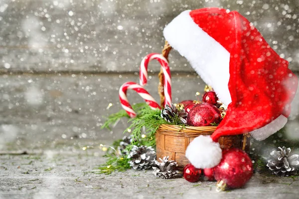 Holiday lesklé složení vánoční koš s míčky, hračky, sladkosti a Borové šišky, santa claus klobouk na vintage dřevěné pozadí — Stock fotografie