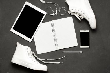 Düz yatıyordu, beyaz spor ayakkabı siyah arka plan ile telefon, kulaklık, tablet, kopya kitap