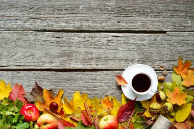 Alt çerçeve sonbaharın kırmızı, yeşil ve sarı yapraklar, meşe palamudu ve elma kahve ya da çay vintage ahşap zemin ile.