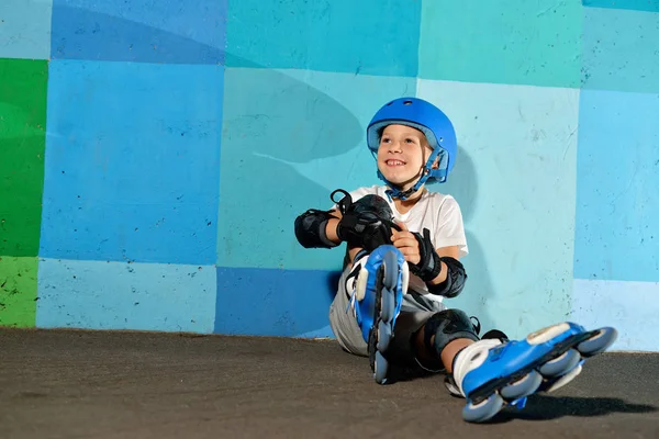 Ładny mały chłopiec lekkoatletycznego na rolki, siedzi pod ścianą blue graffiti — Zdjęcie stockowe
