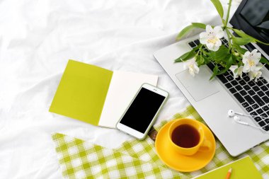 Düz yatıyordu tablet, telefon, çay, dizüstü bilgisayar ve çiçek beyaz battaniye ile yeşil peçete üzerinde sarı Kupası