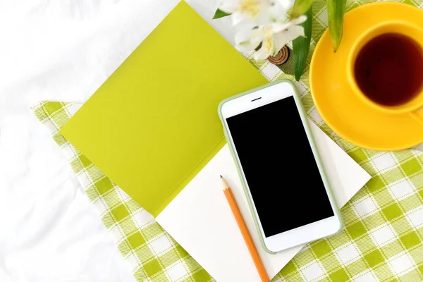 Düz yatıyordu telefon, sarı fincan çay ve yeşil peçete ile beyaz battaniye çiçekler