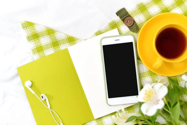 Düz yatıyordu telefon, sarı fincan çay ve yeşil peçete ile beyaz battaniye çiçekler