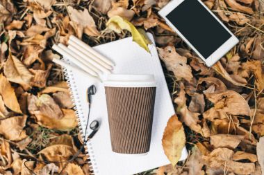 Sonbahar yaprakları, tablet, telefon ve kağıt bardak kahve düz yatıyordu görünümünü. Yukarıdan bacaklar ile