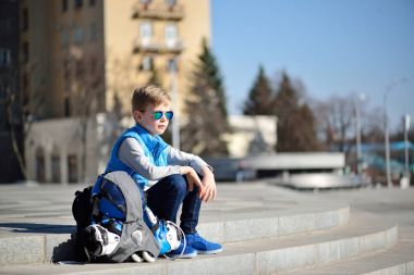 Gri duvara yakın inline paten ve tüm koruma ile açık paten Parkı'nda oturan genç çocuk